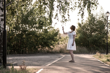 Girl in a white dress on the background of nature and a lamppost	
