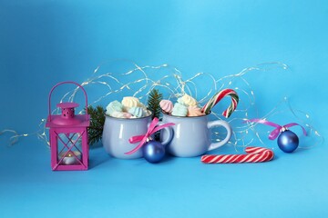 
Merry Christmas, two cups of coffee with meringues and caramel, lantern with a burning candle, fir branches, festive decor, blue color background, winter holidays congratulations concept