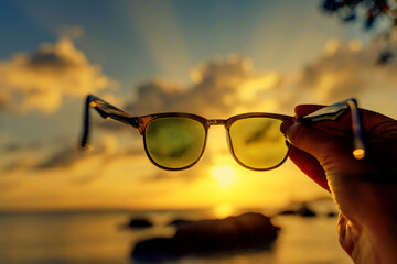 View of the sunset on the tropical sea through sunglasses in hand, abstract conceptual background...