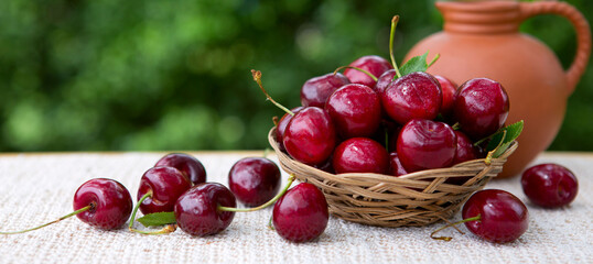 Large red cherries in a basket and a jug of milk isolated on green.