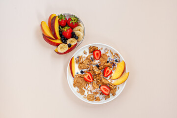 Summer breakfast. Granola and wheat flakes with fruits, berries and milk on a light pink background. View from above.