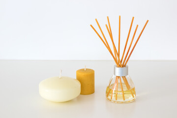 Perfumer with esoteric aromatic oil and wooden sticks, a yellow scented candle and a white floating candle on a white background.