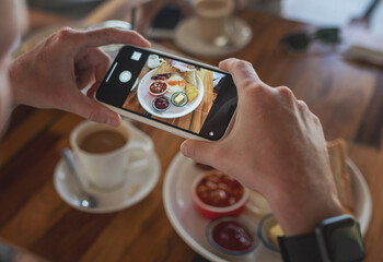 Obraz na płótnie Canvas Photo of food on a smartphone in a cafe, male hands take a picture of a breakfast of scrambled eggs.
