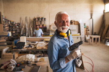 Portrait of a nice old smiling carpenter holding a drill