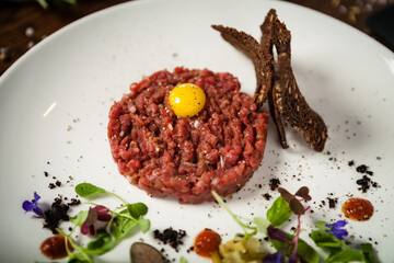 Steak tartare. Horseradish creme, black bread, baguette chips on white plate. Delicious healthy raw meat food closeup served on a table for lunch in modern cuisine gourmet restaurant.