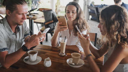 Young group of friends in a cafe drinking coffee, everyone is looking at the smartphone screen, communication problems, modern technologies, a new normal lifestyle