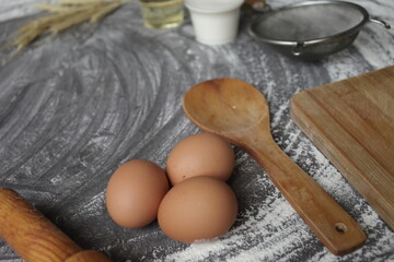 Egg, flour, olive oil, milk, wheat ears, kitchen tool on gray table background.