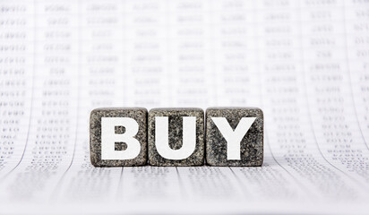 three stone cubes on the background of white financial statements, tables with the word buy. Strong business concept