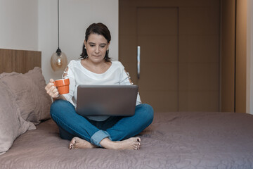 young woman doing home office, holding a cup, with her laptop computer.