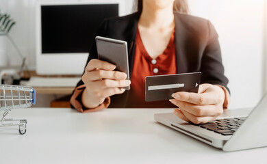 Fototapeta premium businesswoman hand using smart phone, tablet payments and holding credit card online shopping, omni channel, digital tablet docking keyboard computer at office in sun light
