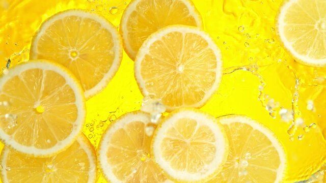 Super Slow Motion Shot of Lemon Slices Falling into Water on Yellow Background at 1000fps.
