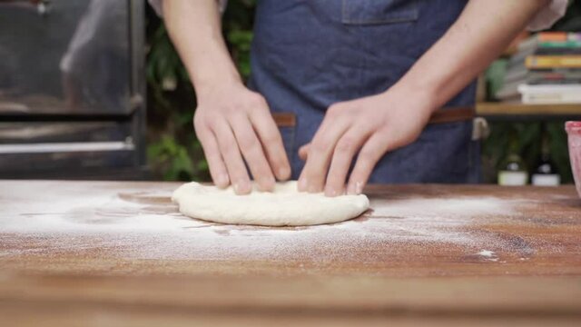 Manos del chef amasando para preparar pizza sobre una mesa de madera. Chef cocinando al aire libre