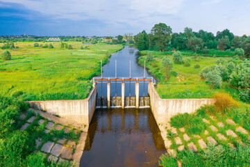 Fototapeta premium Dense on a small river, view of the floodgates. River among fields and meadows, aerial view.