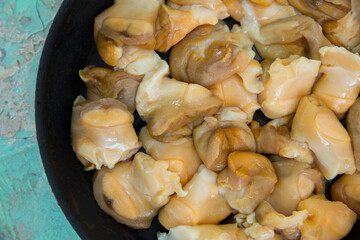 Chopped raw rapana (Rapana pontica) meat in a frying pan on a blue concrete background, close-up.