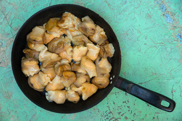 Chopped raw rapana (Rapana pontica) meat in a frying pan on a blue concrete background, close-up.