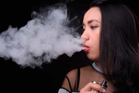 Young beautiful Asian woman vaping against black background