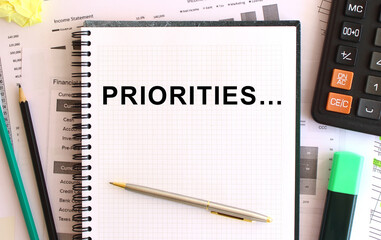 Notepad with text PRIORITIES on a white background, near calculator and office supplies. Business...