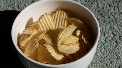 Close up and isolated photo of rustic potato chips in a white ceramic bowl. Concept photo for snacks and unhealthy foods.
