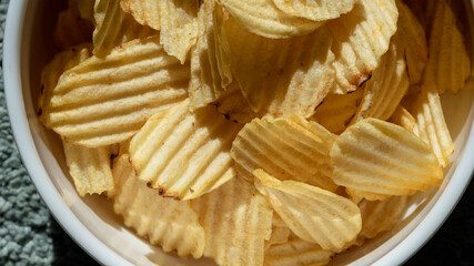 Close up and isolated photo of rustic potato chips in a white ceramic bowl. Concept photo for snacks and unhealthy foods.

