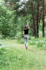 young woman with a tail of hair in a black t-shirt and gray jeans in the woods holding blue wildflowers in her hands