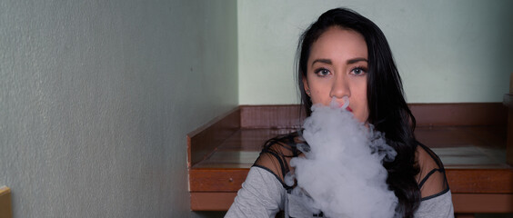 Young beautiful Asian woman vaping at home