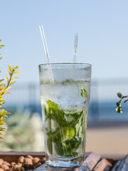 Closeup glass of non-alcoholic mojito cocktail with lime and mint decorated with a two tubes at bar background.