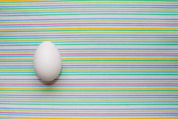 white chicken egg on a bright striped table cloth. Design for poultry industry, production of eco bio natural food. Free space for text. minimalistic top view. design for banners, cards.