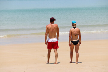 Couple going to swim in the sea, rear view. Girl in bikini and man in shorts walk together by sand, romantic holiday and beach vacation