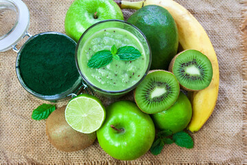 Fototapeta na wymiar Green smoothie, fruit and spirulina on jute fabric, healthy food theme, protein shakes