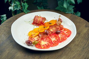 Tomato carpaccio with capers and bacon in a white plate on a wooden background. Italian appetizer