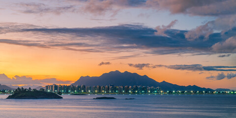 Foto panorâmica do pôr-do-sol na Praia de Camburi mostrando a Mata da Praia, as luzes do calçadão e o Mestre Álvaro ao fundo. Vitória, Estado do Espírito Santo, Brasil.
