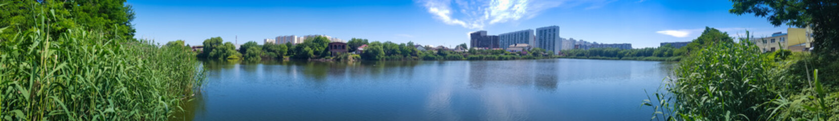 Fototapeta na wymiar panorama city high-rise buildings on the shore of the lake thickets of green trees bushes. rest within the city city infrastructure park square recreation area