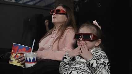 Obraz premium Mother with her daughter are watching 3d film in cinema. Emotion - surprise