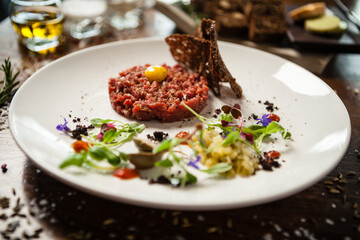Steak tartare. Horseradish creme, black bread, baguette chips on white plate. Delicious healthy raw meat food closeup served on a table for lunch in modern cuisine gourmet restaurant.