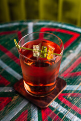 A transparent cocktail in a highball glass with a big ice cube garnished with gummy bears