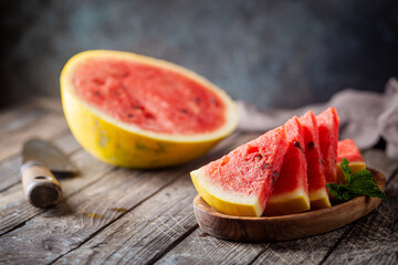 watermelon with yellow peel and watermelon slices in a wooden background.