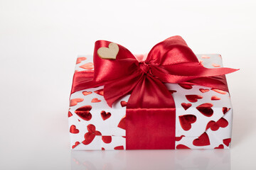Gift box wrapped in white paper with red heart texture. And wrapped in a pink ribbon.