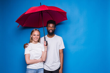 Happy mixed couple holding an umbrella on blue background