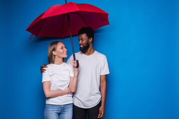 Happy mixed couple holding an umbrella on blue background