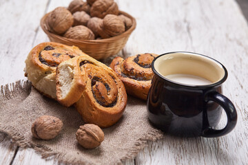Basket of homemade buns with jam, served on old wooden table with walnuts and cup of milk
