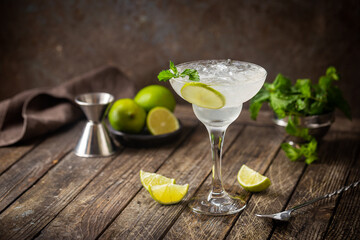 Cocktail margarita garnished with lime and mint on wooden background