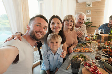 Portrait of mature man making selfie portrait of his big family while they sitting at the table during dinner at home