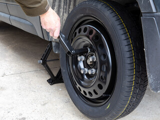 a man using an OEM  tire wrench to tighten the wheel lug nuts to install a compact spare tire of a car on a jack