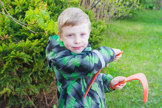 Baby boy blond European holding two orange boomerangs. The child wants to launch bright boomerangs into the sky.