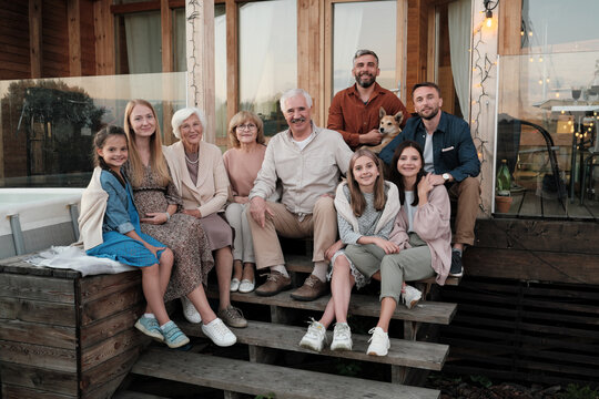 Portrait of big happy family sitting on the porch and smiling at camera they gathered in their big house in the country