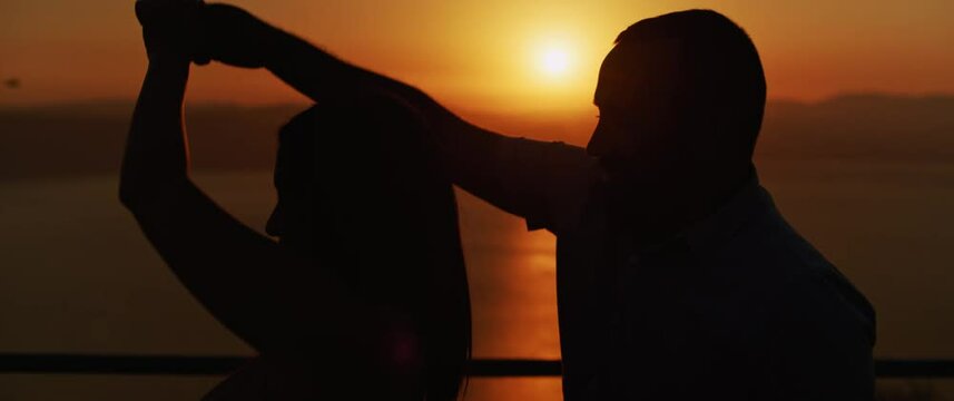 Close up of a young couple dancing and having fun at sunset, spending a romantic evening together. Slow motion.  
