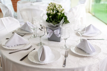 Mesa de convidados com forro branco, pratos, copos, guardanapos e um vaso com flores ao centro. - obrazy, fototapety, plakaty