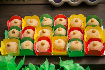 Docinhos, em papéis coloridos e arranjados sobre mesa decorada para festa.