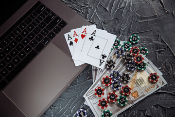 Stacks of poker chips, money banknotes and playing cards on a laptop computer. Online casino concept.