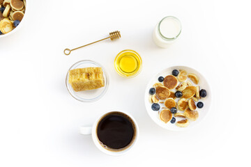 Mini Pancake cereal with two different honey and honeycomb, yogurt, milk and blueberry on white plate and black coffee on white cup.